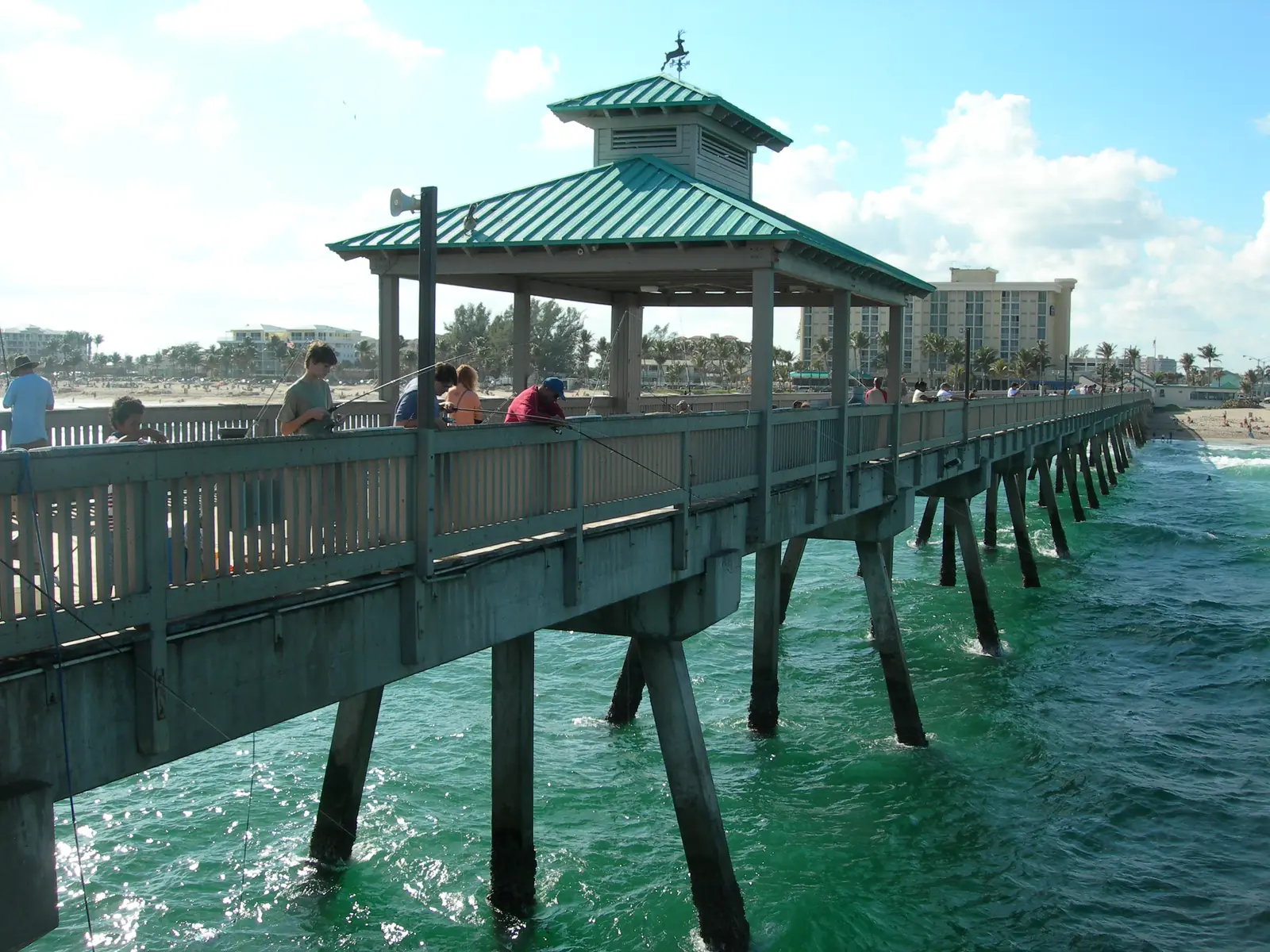 The end of the Deerfield Beach pier with its green-roofed shelter and weather vane, anglers along the rail and green water below.