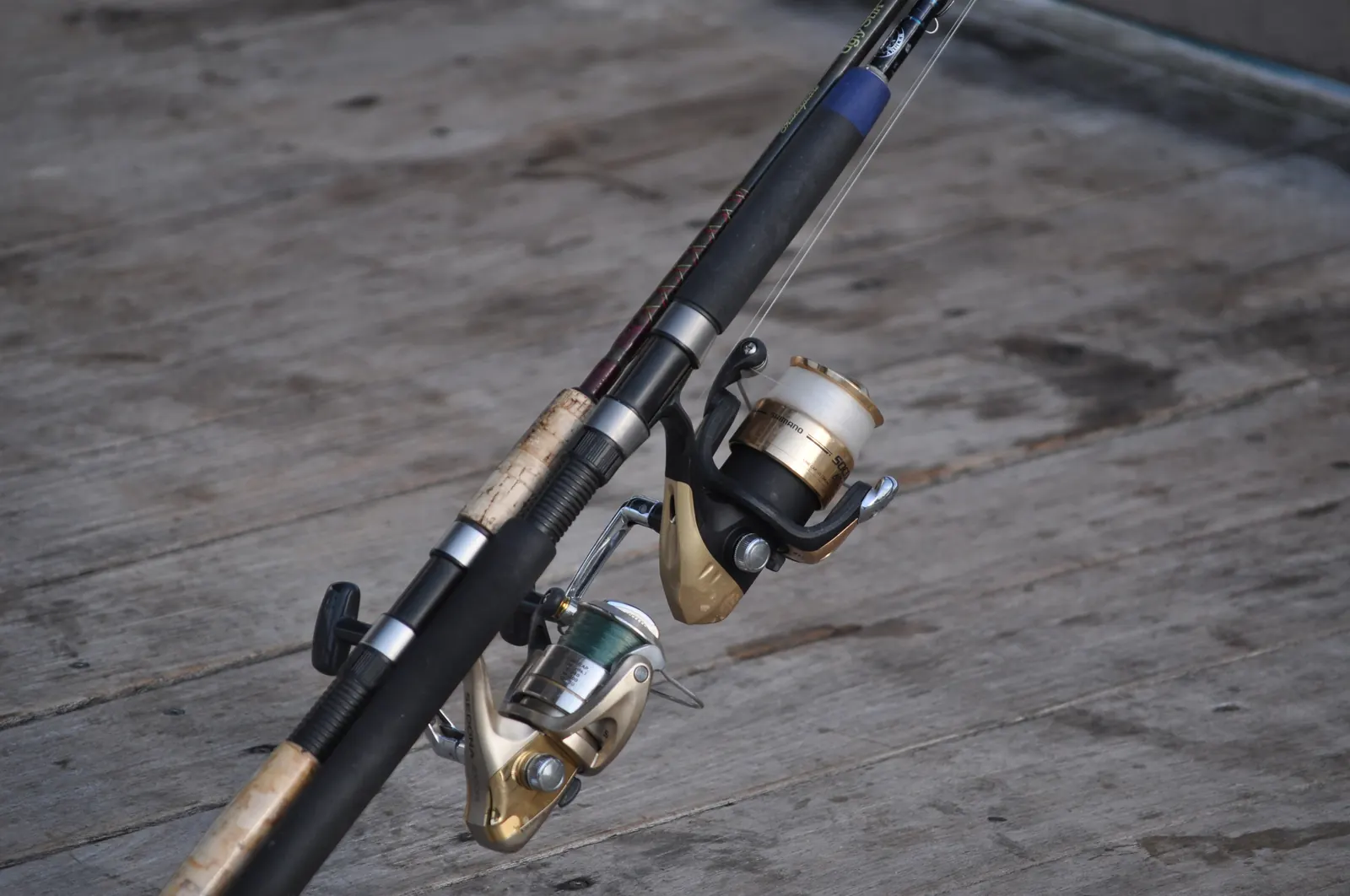 Close-up of two spinning reels on fishing rods resting on the weathered boards of the Deerfield Beach pier.
